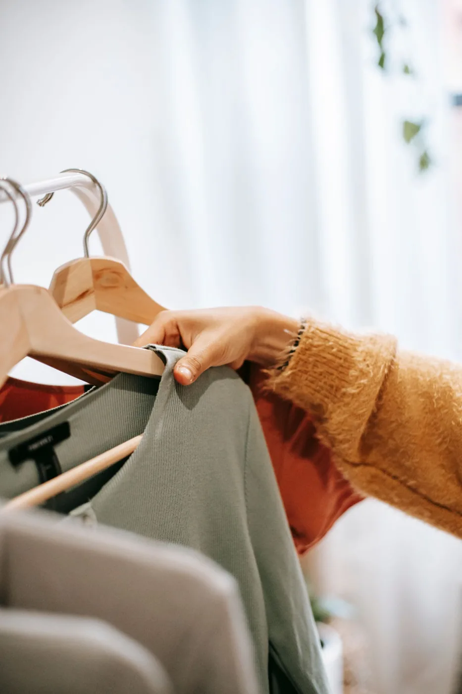 Woman selecting clothes from wooden hangers on a wardrobe rail