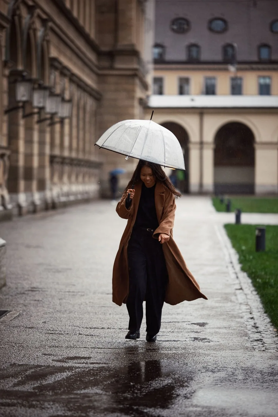 Woman walking with an umbrella and brown coat on a rainy city street